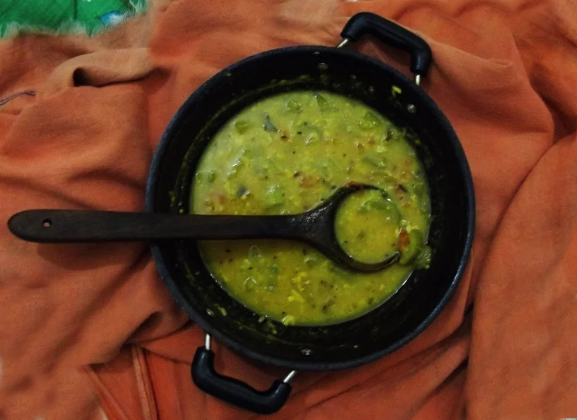 Dalma in a black handled pan with a ladle, on an orange cloth.