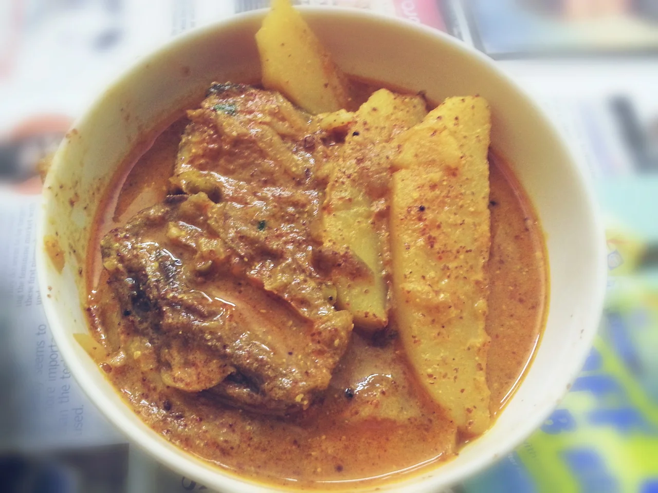Fish pieces and long potato wedges in mustard-coloured gravy in a white bowl.
