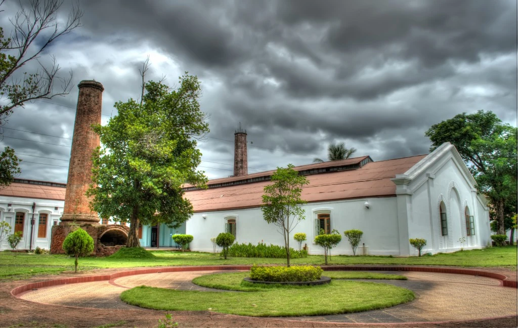 A white museum building, brick chimneys and circular garden beneath a cloudy sky.