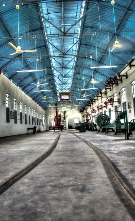 Rails curve through a tall workshop hall, with machinery and overhead wheels along its right-hand side.