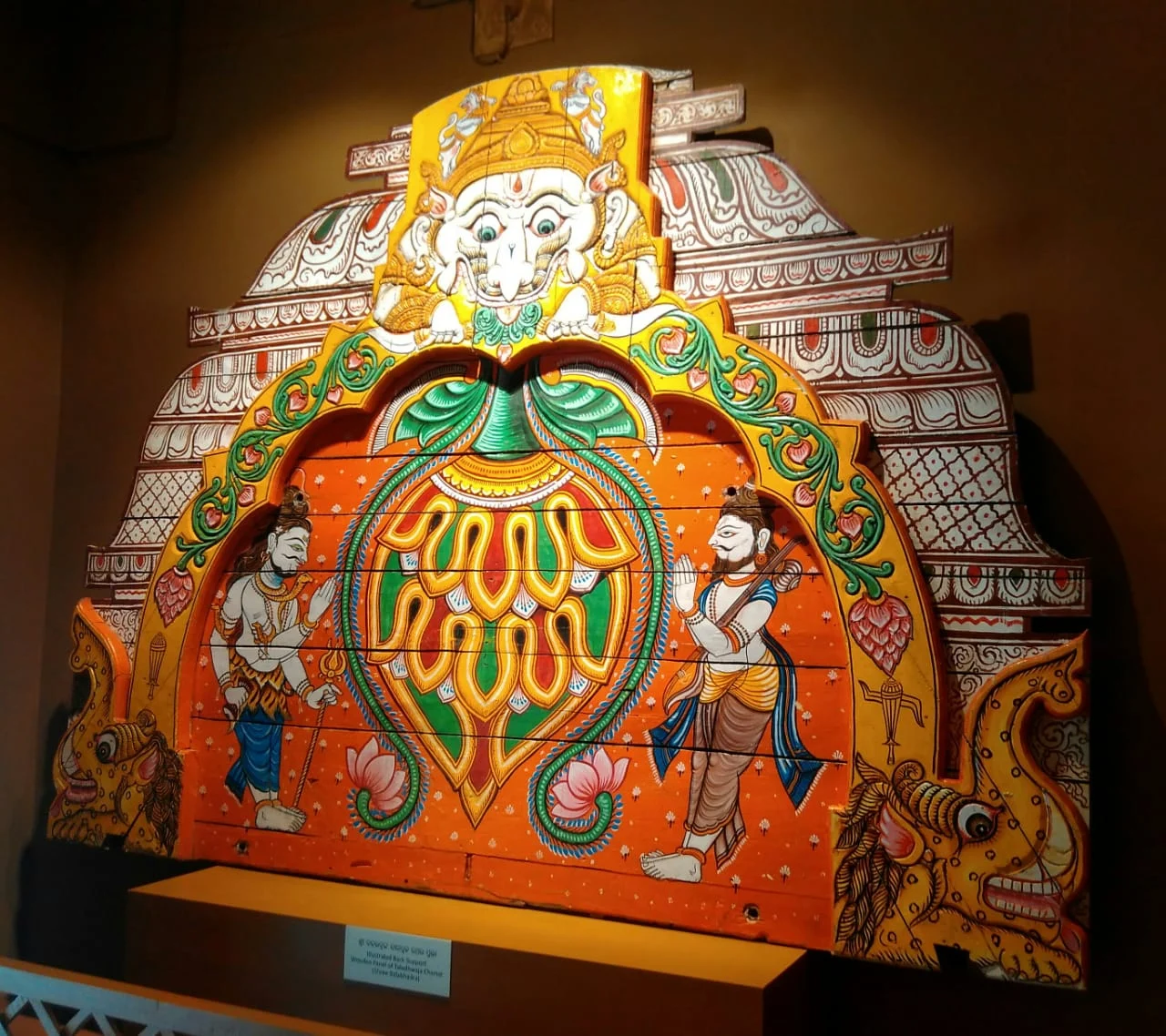 A painted wooden chariot panel with floral forms, figures and a central decorative arch.