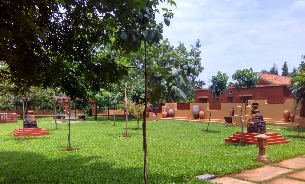 Trees, lawn and earthen-coloured museum buildings, with pots and sculptural displays outdoors.